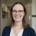 Nicole Scienza, in glasses and a blue sweater, smiles at the camera.